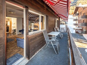 Eine Holzhütte mit überdachter Außenbestuhlung, einem sichtbaren Eingang und Blick auf einen verschneiten Berg.