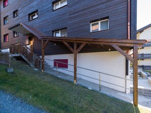 Un edificio de varios pisos con un espacio exterior cubierto, una escalera y una puerta de garaje roja.