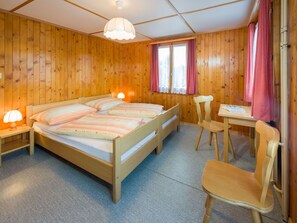 Ett rum med träpanel, en säng, två sänglampor, ett skrivbord med en stol och ett fönster med gardiner.