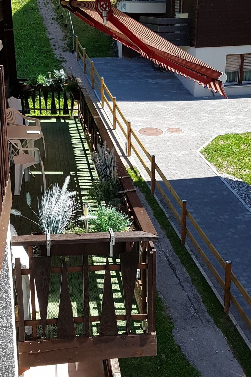 Un espacio de estar al aire libre cubierto con valla de madera, plantas en macetas y un sendero que lleva a un edificio.