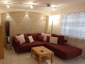 Ein Wohnzimmer mit einem roten Modulsofa, einem Holztisch, einer Wand mit Steinverkleidung und einem Fenster mit Jalousien.