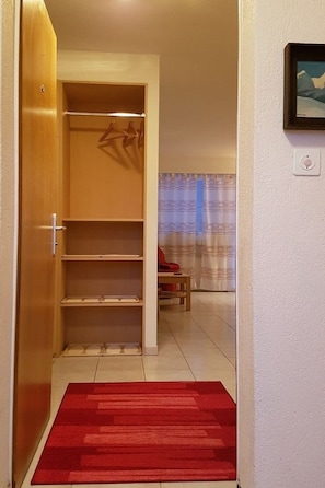 Ein Zimmer mit einem Holzschrank, einem roten Teppich, einem Tisch mit Stuhl und einem fenster mit Vorhängen.