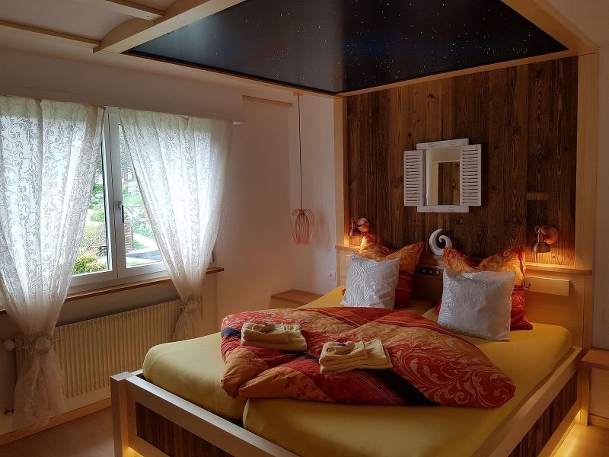 Ein Schlafzimmer mit einem Bett, Vorhängen, einer Decke mit Sternenhimmel und einer Holzwandverkleidung.