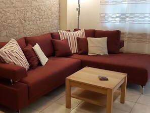 Un sofá seccional rojo con múltiples almohadas y una mesa de centro de madera en una habitación con pared de piedra y una ventana con persianas.