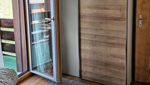 Quarto com porta de vidro deslizante para uma varanda, um guarda-roupa e uma cama com roupa de cama estampada.