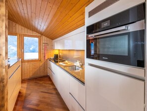 A modern kitchen with wooden walls, a built-in oven, and a window providing a view. - Pumuckl, (Grächen), 2060 by Interhome (Grächen)