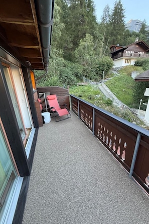 A balcony with a seating area, a view of a forested hillside, and a staircase leading to a building. - Pumuckl, (Grächen), 2060 by Interhome (Grächen)