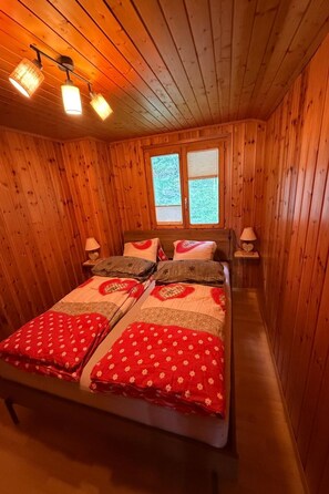 A wooden-paneled room with a bed, two bedside lamps, and a window. - Pumuckl, (Grächen), 2060 by Interhome (Grächen)