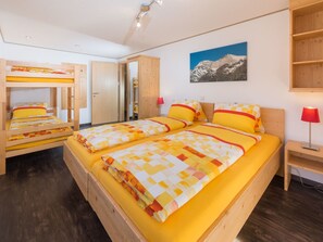A room with bunk beds, a single bed, a mountain painting, a wooden shelf, and a desk with a lamp. - Ferienwohnungen Clarino, AZapartments.ch, B&B, (Grächen), 1285 by Interhome (Grächen)