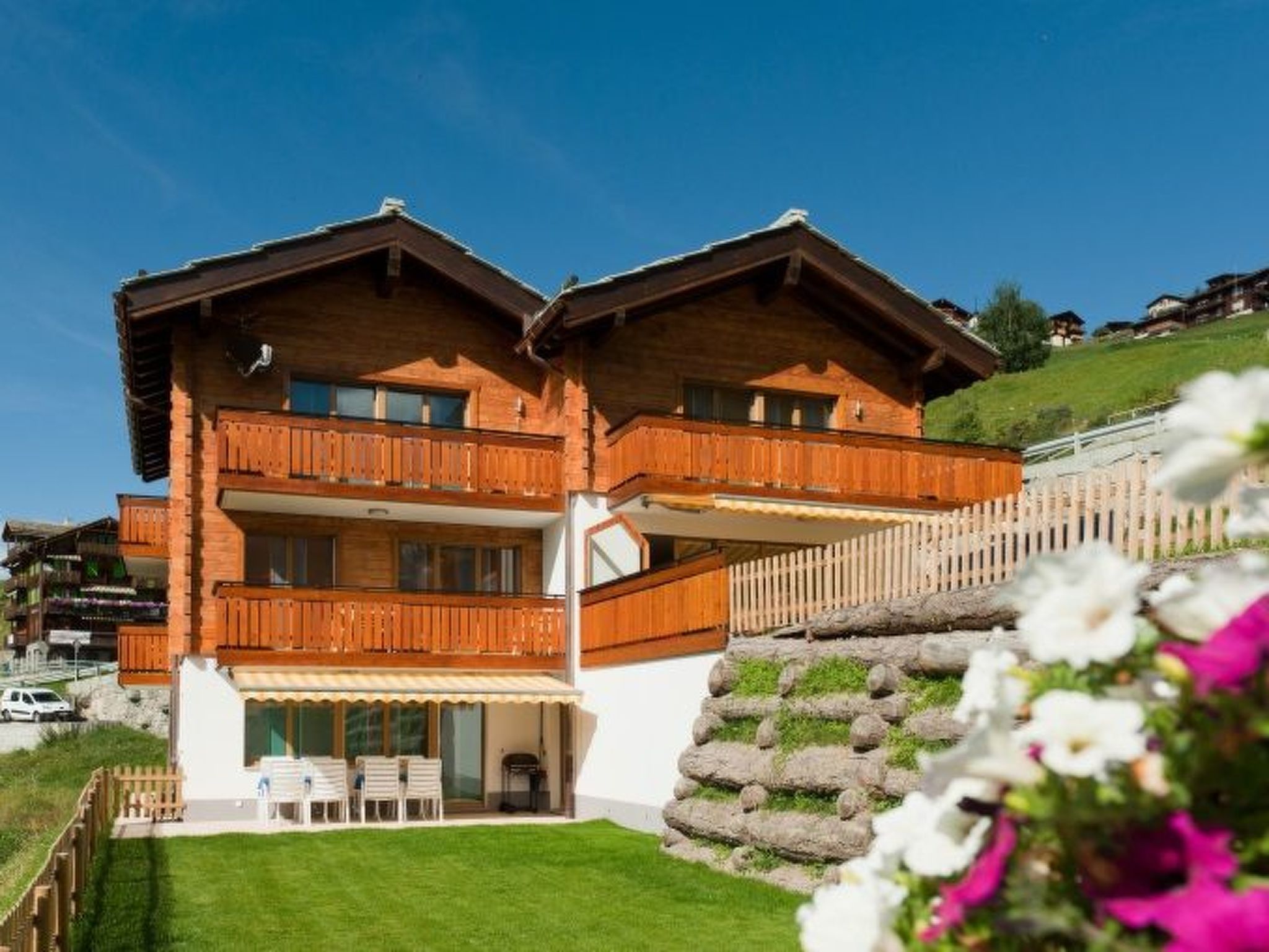 A two-story wooden chalet with balconies, a stone staircase, and a well-maintained lawn.
