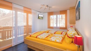 Una camera da letto con un letto, un comodino, una lampada, una ventola a soffitto e una finestra con vista su un edificio.