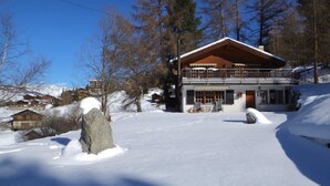 Un edificio de estilo chalé con un balcón grande, rodeado de nieve y árboles.