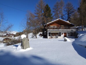 Ein Chalet mit großem Balkon, umgeben von verschneitem Gelände und Bäumen.