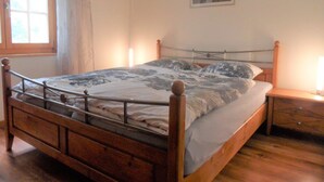 Una cama de madera con estructura metálica, una mesita de noche y una ventana con cortinas.