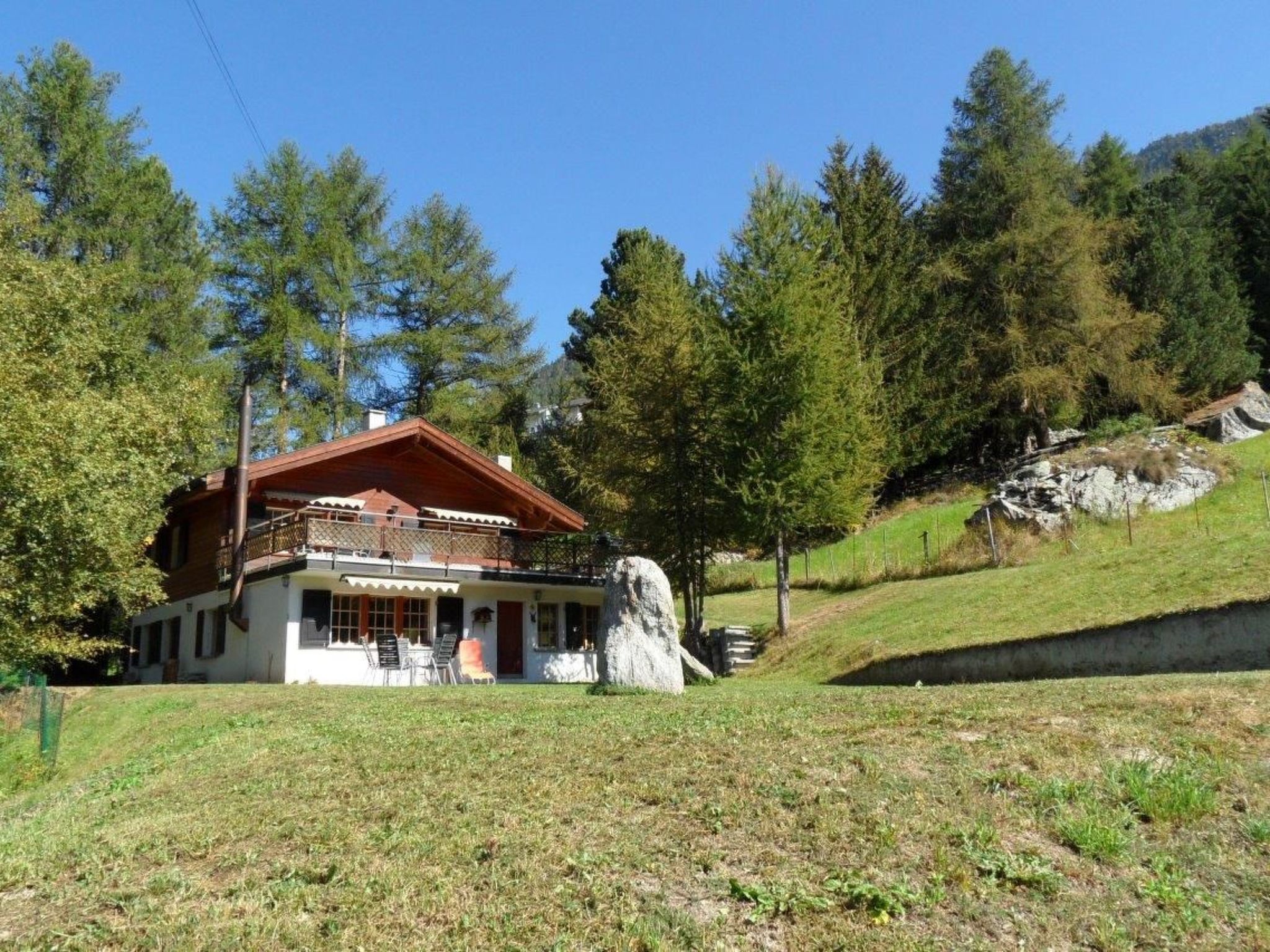 Ein Chalet mit Balkon, umgeben von einer Wiese und Bäumen.