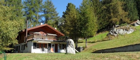 Ein Chalet mit Balkon, umgeben von einer Wiese und Bäumen.