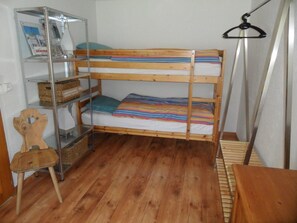Ein Etagenbett mit einer dahinter stehenden Regalwand, ein Holzhocker und eine Pendelleuchte.