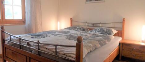 A bedroom with a wooden bed, a nightstand, a window with curtains, and a painting on the wall.