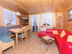 Ein Holzblockhaus-Interieur mit einem Esstisch, Stühlen, einem roten Sofa und einem Fernseher.