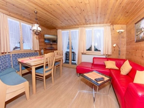A wooden interior with a red sofa, blue chairs, a dining table, and a TV. - Ferienwohnungen Fleurs des Alpes, (Grächen), by Interhome (Grächen)