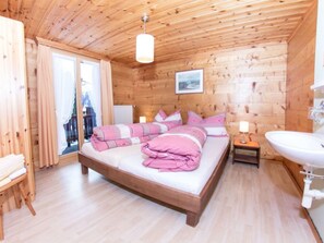 A wooden room with a bed, a bedside table, a lamp, and a view through a window. - Ferienwohnungen Fleurs des Alpes, (Grächen), by Interhome (Grächen)
