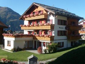 Ein mehrstöckiges Hotel mit Balkonen, die mit Blumen geschmückt sind, einem Schild mit dem Schriftzug 'Miranda' und einer Bergkulisse.