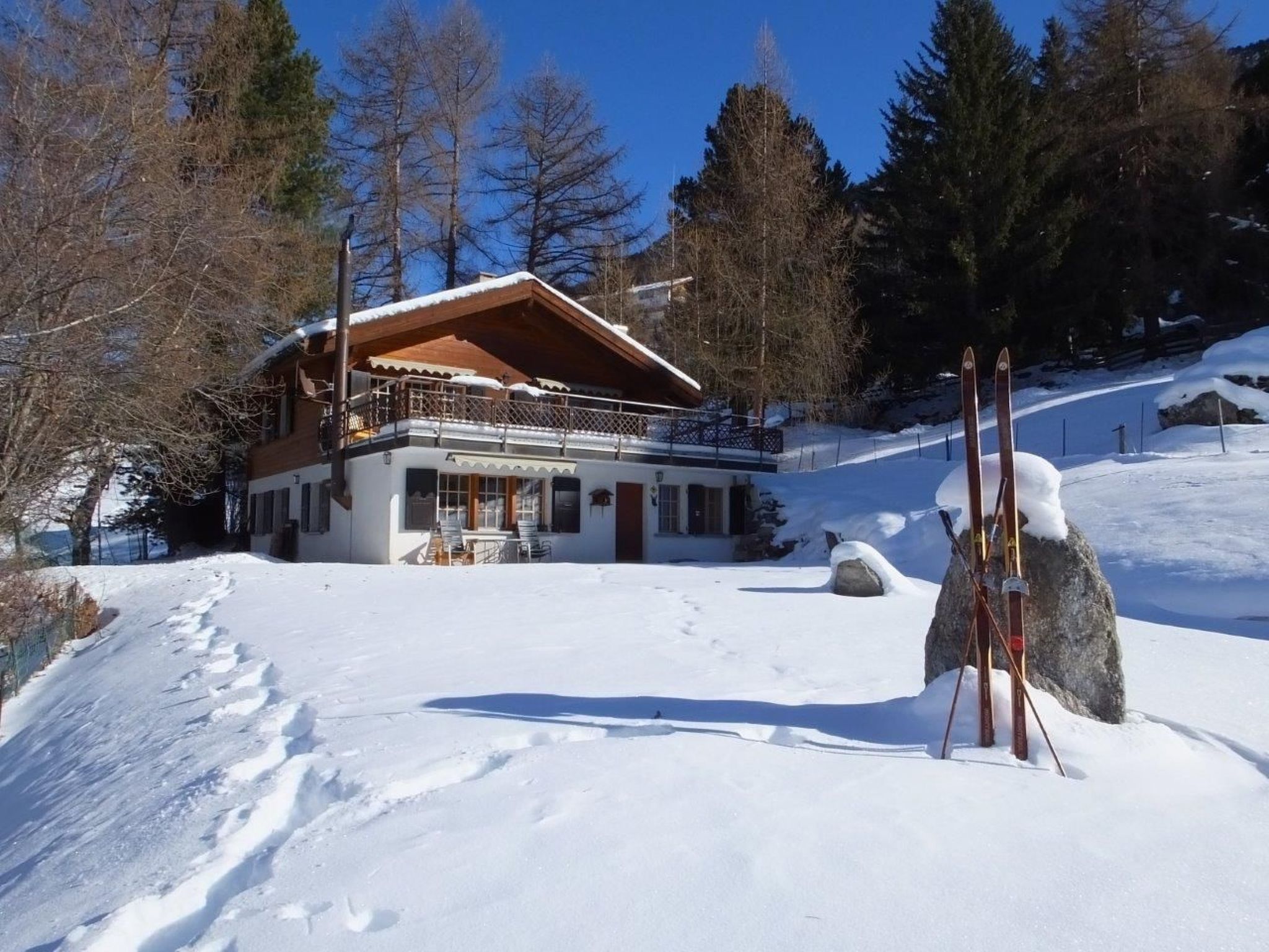 A chalet-style building with a wooden balcony, surrounded by snow-covered ground and trees.