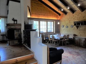 Ein rustikales Interieur mit Kamin, Holzbalken, einem Essbereich und einer Treppe.