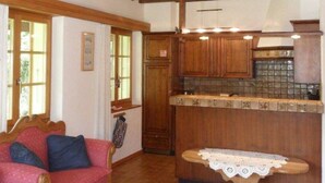 Ein rustikales Interieur mit Holzbalkendecke, einem gemütlichen rotem Sofa, einem kleinen Tisch mit Spitze und einer Küchenzeile mit Holzschränken.