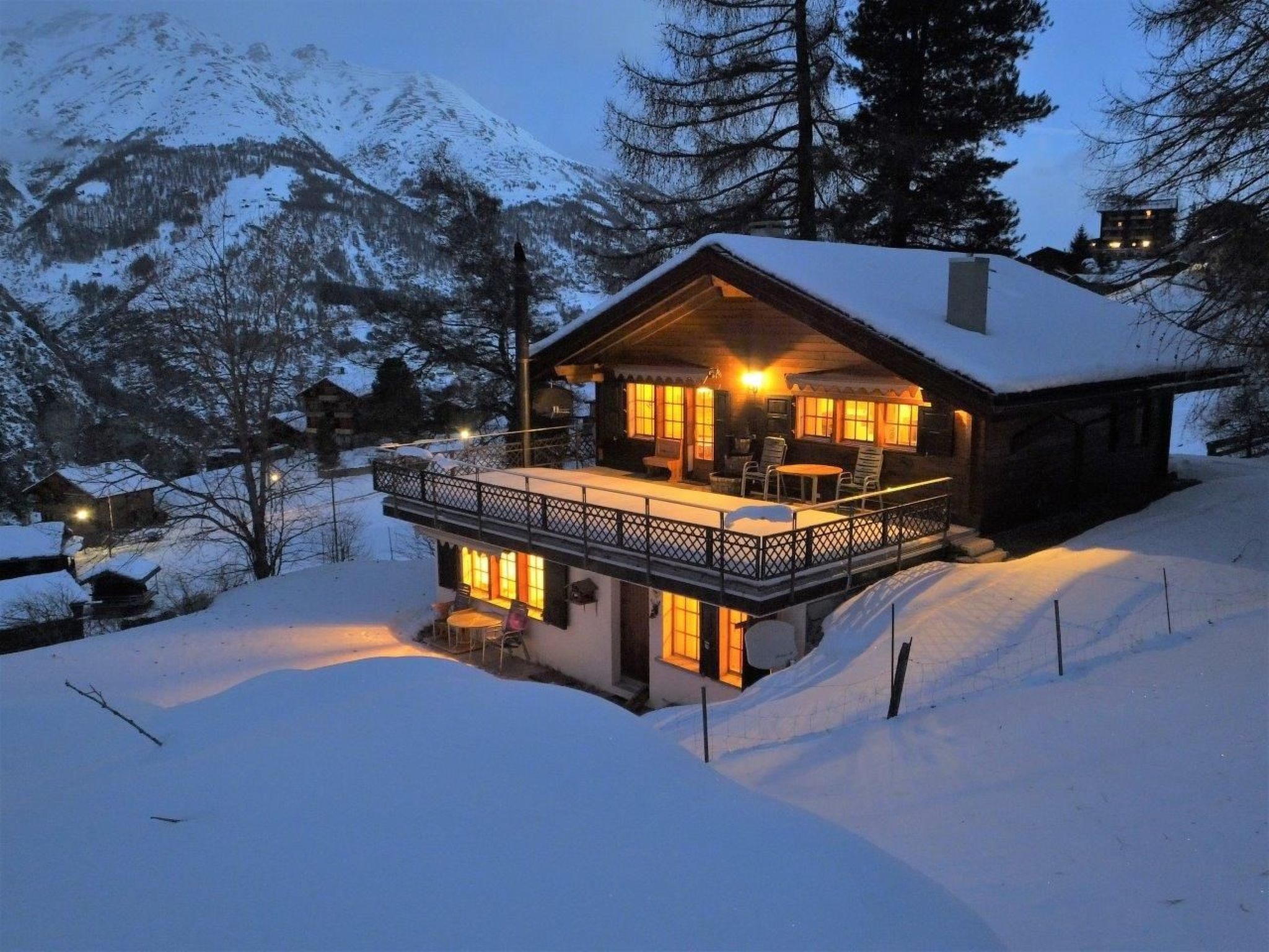 A snow-covered house with a balcony, surrounded by trees and mountains.