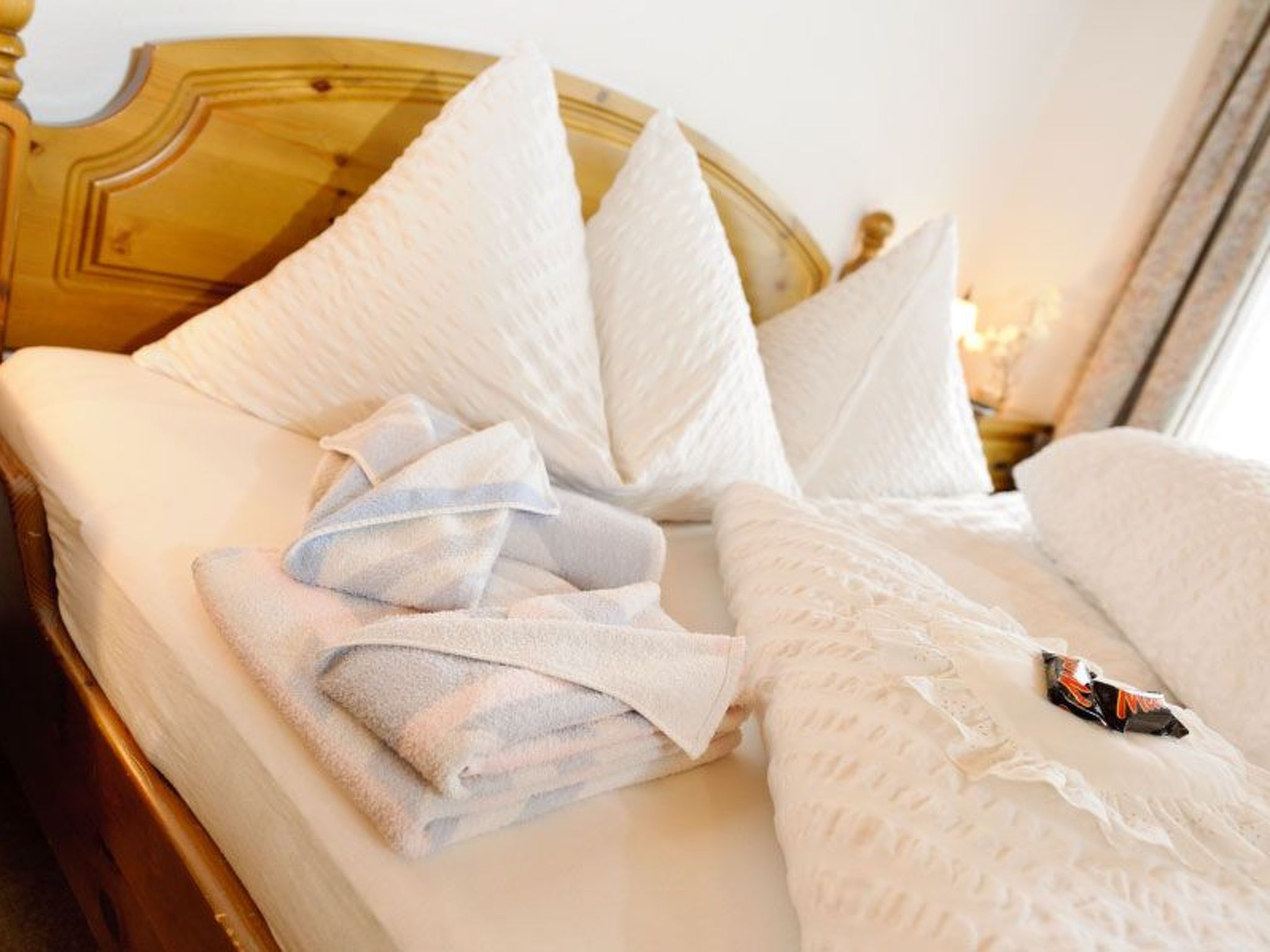 Un letto con lenzuola bianche, un asciugamano piegato e una coperta.