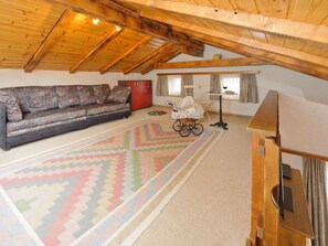 Ein geräumiges Dachzimmer mit Holzbalkendecke, einem gemusterten Teppich, einer Couch, einem roten Schrank und einem Fahrrad.