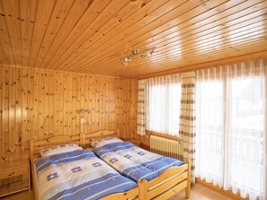 Ein Zimmer in einer Holzhütte mit zwei Betten, einem Fenster mit Vorhängen und einer Decke mit Holzbalken.