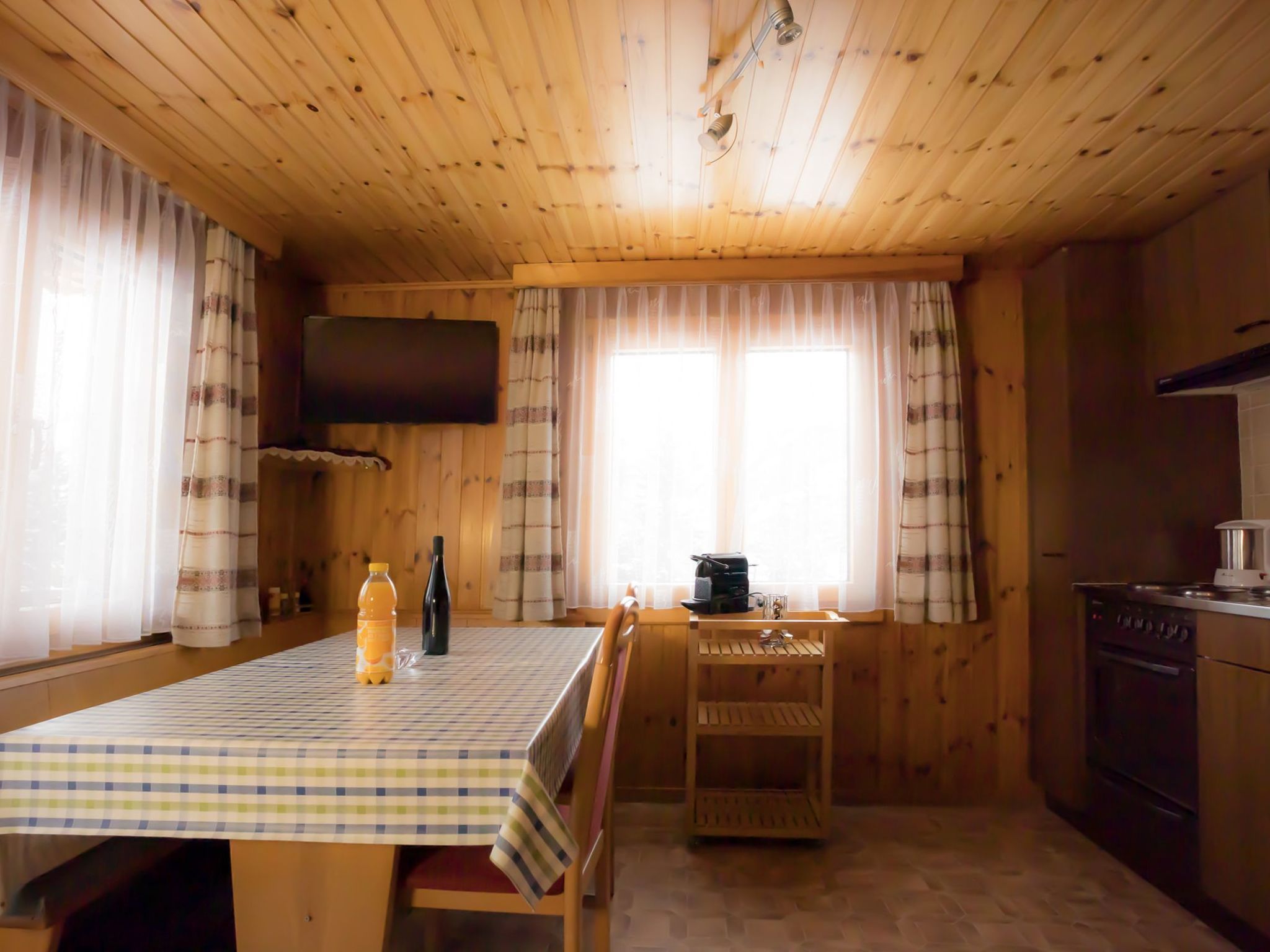 Ein Holzblockhaus-Interieur mit Esstisch, Stühlen, einer Küchenzeile und einem an der Wand befestigten Fernseher.