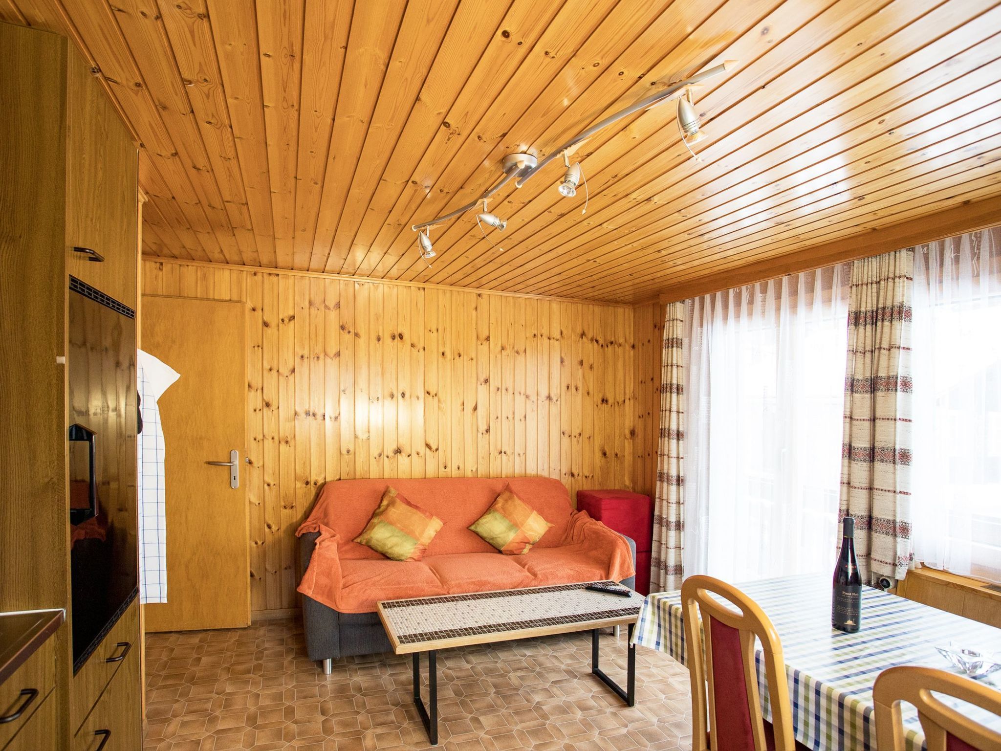 Een kamer met houten lambrisering, een bank, een tafel en een raam met gordijnen.