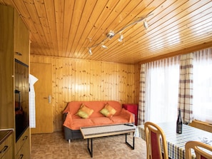 Ein Zimmer mit Holzwandverkleidung, einem Sofa, einem Tisch und einem mit Vorhängen drapierten Fenster.