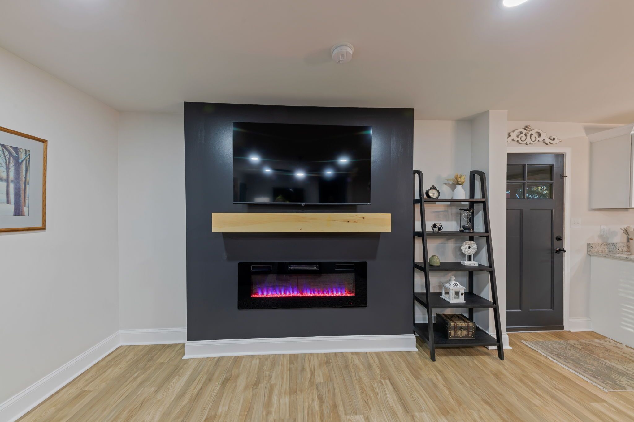 Un salon moderne avec une cheminée, un téléviseur fixé au mur et une étagère en bois.