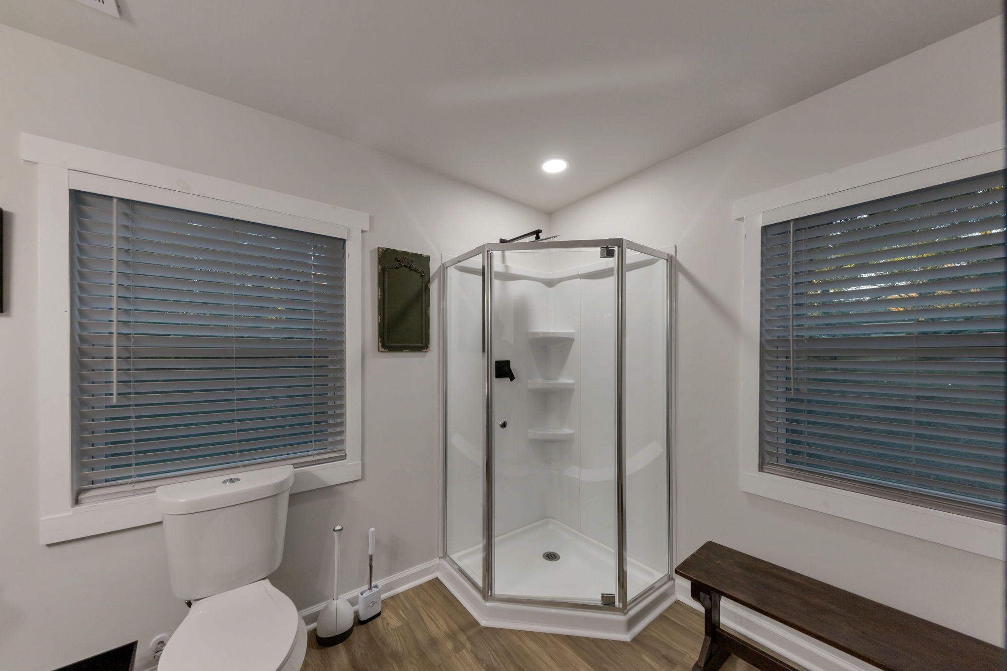 Un baño con cabina de ducha de vidrio, inodoro y banco.