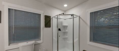 Un baño con cabina de ducha de vidrio, inodoro y banco.