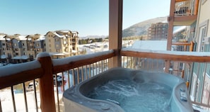 Ein Whirlpool auf einem Balkon mit Blick auf einen verschneiten Berg und Gebäude.