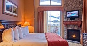 Una habitación de hotel con cama, chimenea, televisión y vistas al exterior.