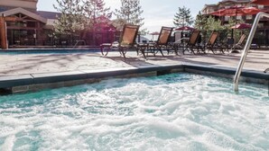 Una piscina con un jacuzzi, sillas de descanso y sombrillas.