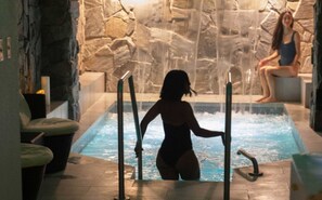 Una mujer en traje de baño junto a una piscina, con un muro de piedra al fondo.