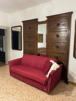 A red sofa in a room with a large wooden wardrobe and a mirror.