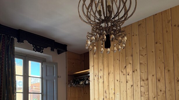 A bedroom with a wooden wall, a chandelier, a bed with white bedding, and a window with curtains. - Viale del Re 33: A Summer Fairy Tale Between the Sea and the Theater (Reggio Calabria)