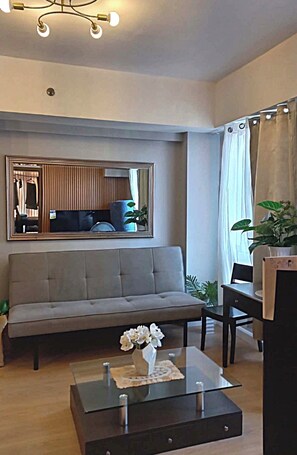Un salon avec un canapé, une table basse sur laquelle est posé un vase, un miroir et une fenêtre avec des rideaux.