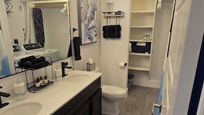 Une salle de bain moderne dotée d’un grand miroir, de deux vasques, de toilettes et d’un dressing.