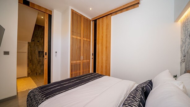 Een slaapkamer met een bed, een houten kledingkast en een badkamer die door een open deur zichtbaar is.