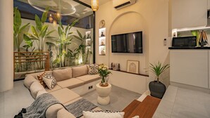 Een moderne woonkamer met een bank, salontafel en een groot raam met planten.