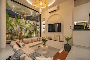 A modern living room with a sofa, coffee table, and a large window with plants. - Villa Scorpia 1 Bingin (Pecatu)